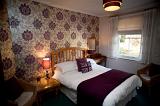Comfortable bed in a bedroom with vintage wallpaper with a large floral design and a lamp burning on the bedside table