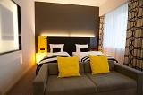 Modern designer bedroom with striking black and white decor with colorful yellow highlights and a couch at the foot of a double bed illuminated at night