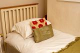 Single bed with white bed linen and decorative gold and red cushions with a simple wooden headboard, closeup view