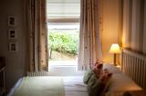 Homely bedroom with a double bed and window looking out over a leafy green garden illuminated by a bedside lamp