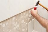 Man removing old white ceramic wall tiles with a hammer and screwdriver as he prepares to redecorate his house