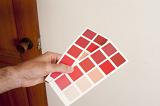Man holding two cards of colorful red paint swatches to a wall, close up view of his hand in a renovations, interior decorating or DIY concept