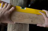 Man using a spirit level to level a piece of wood on the horizontal plan while doing carpentry and DIY renovations