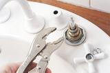 Man doing home plumbing maintenance fixing a faucet or tap on a sink with a mole grip wrench