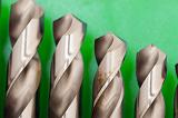 Close up of the tips of a set of metal steel spiral woodworking drill bits in descending size on a green background with copyspace