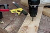 Drilling a hole in a plank of wood with an electric handheld power drill with a close up view of the steel bit and sawdust as it penetrates the wood in a carpentry workshop or DIY concept