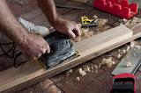 Woodworker, carpenter or joiner sanding a plank of wood with an electric sander on a brick floor in a DIY concept