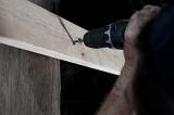 Man fixing wood to a support with a screw using a screwdriver attachment on his electric drill, close up of his hand and the drill bit