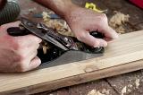 Man planing a plank of wood with a handheld manual planer in a DIY, renovation and woodworking concept, close up view of his hands