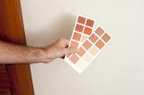 Man holding up red paint swatches on cards in front of a white wall in a house as he chooses the correct color for his interior decorating and renovation