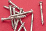 Fully threaded silver metal woodworking screws piled randomly on a red background in a DIY concept, close up view from above