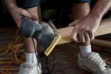 Handyman doing joinery using an electric sander to smooth the surface of a plank of wood before installing it in a house, close up of his hands