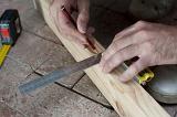 Man marking a square for a right angle cut on a plank of wood in his woodworking workshop as he renovates his home