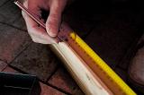 Carpenter carefully measuring a length of wood with a tape measure repeating his measurement a second time for accuracy