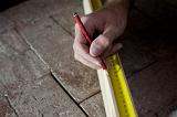 Measuring the length of a plank of wood using a builders tape measure and pencil, close up of the carpenters hand