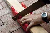 Man using a mitre box with guides for specific angles of cut to saw wood on a brick floor in a DIY concept