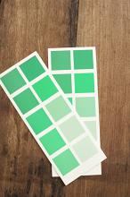 Two paint color swatch cards in green for selecting the correct hue for interior decorating lying on a wooden surface in a DIY concept