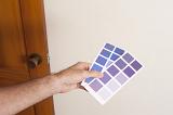 Man holding up blue paint swatches on cards against a white wall as he plans his new color scheme while interior decorating