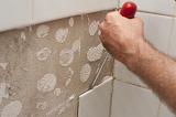 Man prising loose old wall tiles with a screwdriver as he renovates his home in a DIY concept