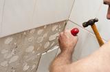 Workman removing old wall tiles with a hammer and screwdriver after first removing the grout with an oscillator
