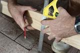 Man marking a right angle cut on a plank of wood as he renovates his house, close up view of his hands and the tool