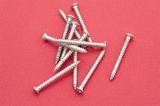 Pile of threaded metal wood screws on a red background conceptual of DIY, carpentry, renovations or construction