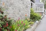 Cottage country garden with summer flowers in a flowerbed along an old stone wall in a receding view