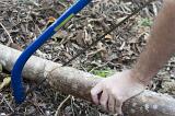 Man cutting a tree branch lying on the ground in a garden with a pruning saw, close up of the tool and his hand