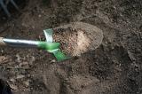 Digging in the garden with a green metal shovel or spade turning over the earth for planting in spring, close up of the blade