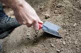 Man digging in his garden in the dry soil with a small trowel as he prepares to transplant spring seedlings, closeup of his hand