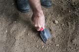 Man digging in the ground in the garden with a small trowel, closeup high angle view of his hand