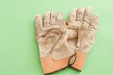 Pair of used leather gardening gloves laying on a green background with copyspace, viewed from above