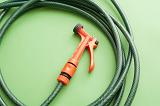 Orange plastic garden sprayer attached to the end of a neatly coiled green hosepipe on a green background