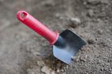 Small garden trowel with a red plastic handle in dry soil ready for digging over the earth