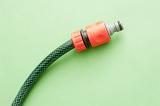 Universal plastic connector on a garden hose for quick attachment to taps and accessories, on a green background with copyspace
