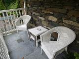 White painted wicker table and armchairs on an outdoor patio or veranda enclosed by a railing on a stone house