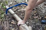 Man clearing up in the garden sawing a log lying on the ground with a pruning saw, close up of his arms and the saw