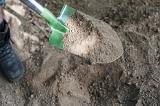 Digging in garden soil with a spade or shovel, close up view of the green metal blade
