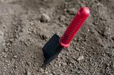 Garden trowel with a red plastic handle inserted into the ground ready to dig over the soil, high angle view