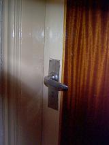 Detail of Silver Colored Door Handle on Closed Door with Large Curtained Window, Partially Obscured by Shadow