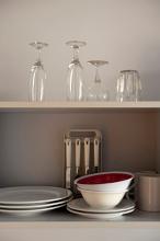 Assorted crockery and glassware stacked on an open wooden kitchen shelf