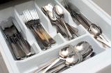 Open cutlery drawer with inside dividers filled with silver stainless steel knives, forks, spoons and teaspoons for eating