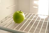 Interior of a small domestic refrigerator with a single green apple on the wire shelf