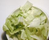 Closeup of a white bowl of shredded iceberg lettuce over white background