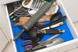 Open kitchen drawer with an assortment of cooking utensils including a rolling pin, grater, scissors and spoons
