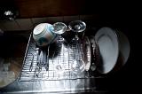 Washing up consisting of plates, bowls and glasses draining on the draining section of a stainless steel kitchen sink