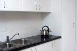 Kitchen worktop with kettle and stainless steel double sink and white cupboards.