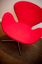 Red designer armchair in a retro style with a moulded frame and steel base, close up view
