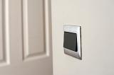 Modern silver framed plastic light switch on a white wall alongside a white painted wooden paneled door