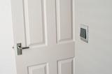 Close up of an open white wooden paneled living room door with a light switch on the wall